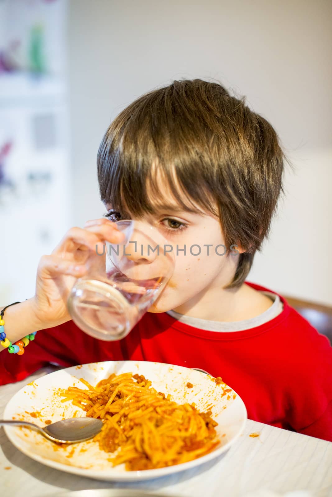 child drink water and eating spaghetti at home