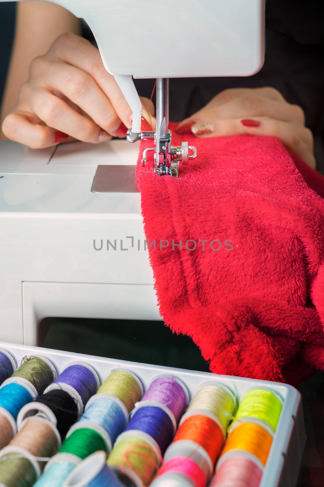 Young woman sewing fabric on sewing machine,sewing process in the phase of overstitchin,colored spools.