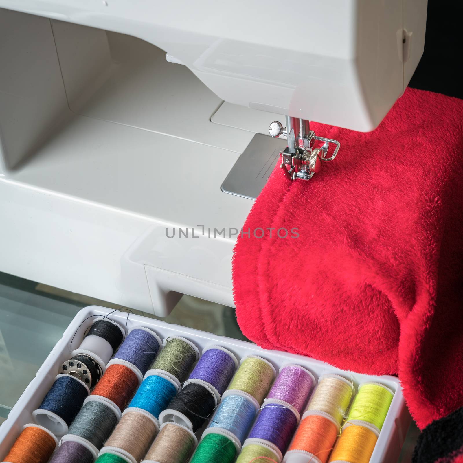 sewing machine and red cloth, sewing process in the phase of overstitching,colored spools.