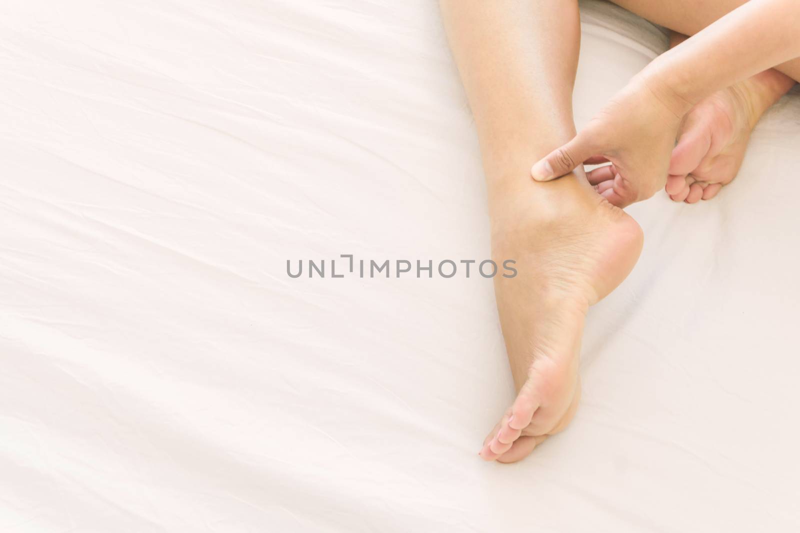 Woman hand holding ankle with pain on white bed, health care and medical concept