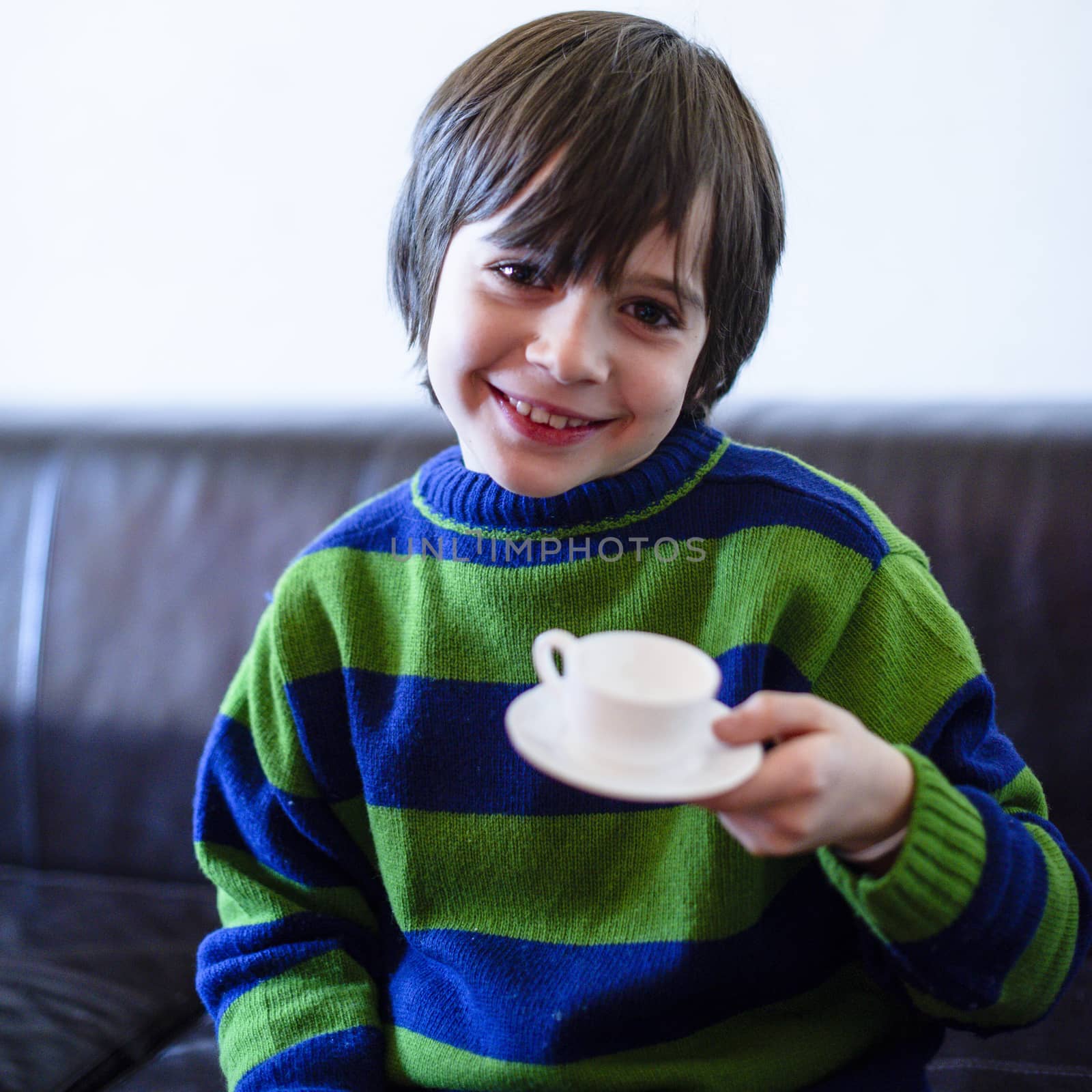 child plays, drinking tea on the sofa at home, lit by the window