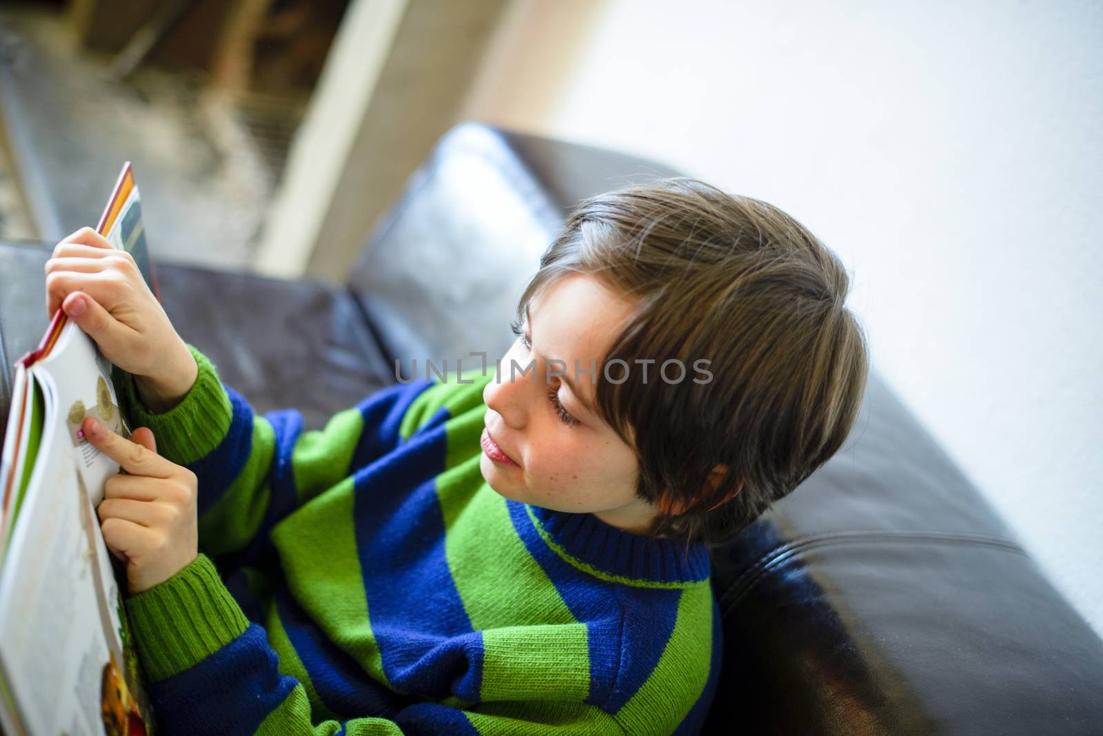 child reads a book sitting on the couch