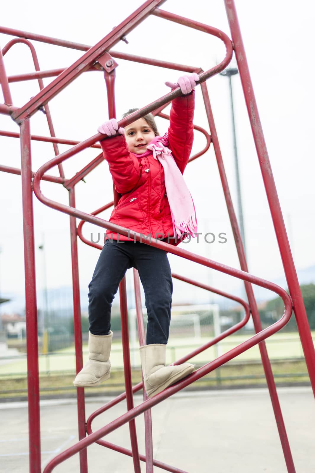 little girl climbs on iron frame of a basketball hoop in an outdoor basketball court