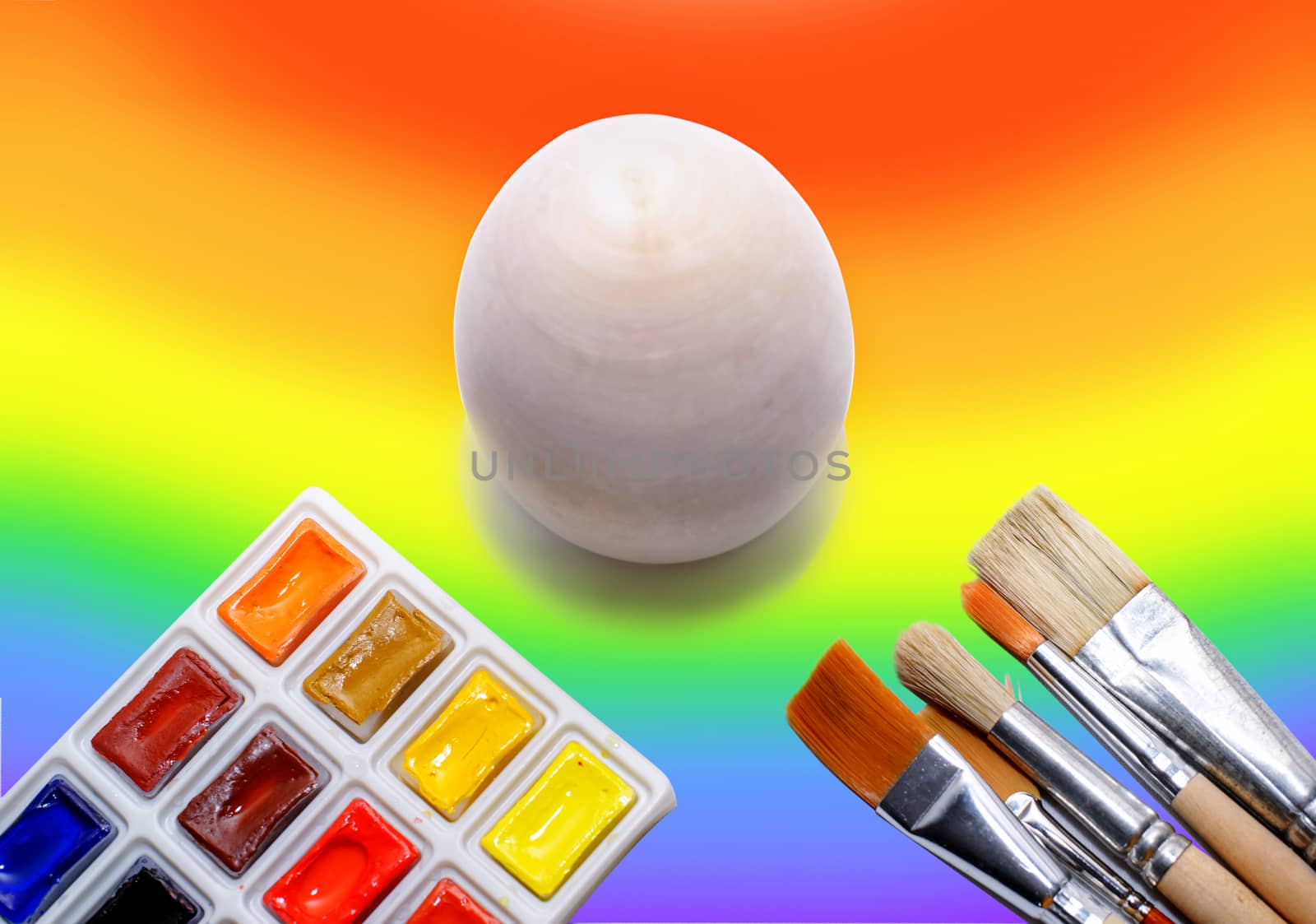 Wooden not painted egg on the background of a rainbow and a brush with paints, the concept of coloring the world with paints.