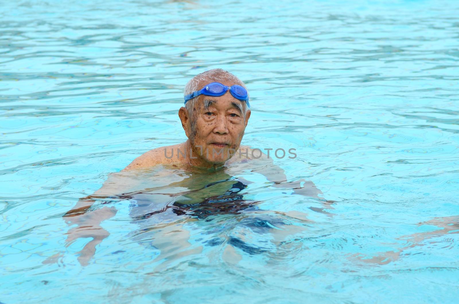Asian senior man in a swimming pool, looking at camera
