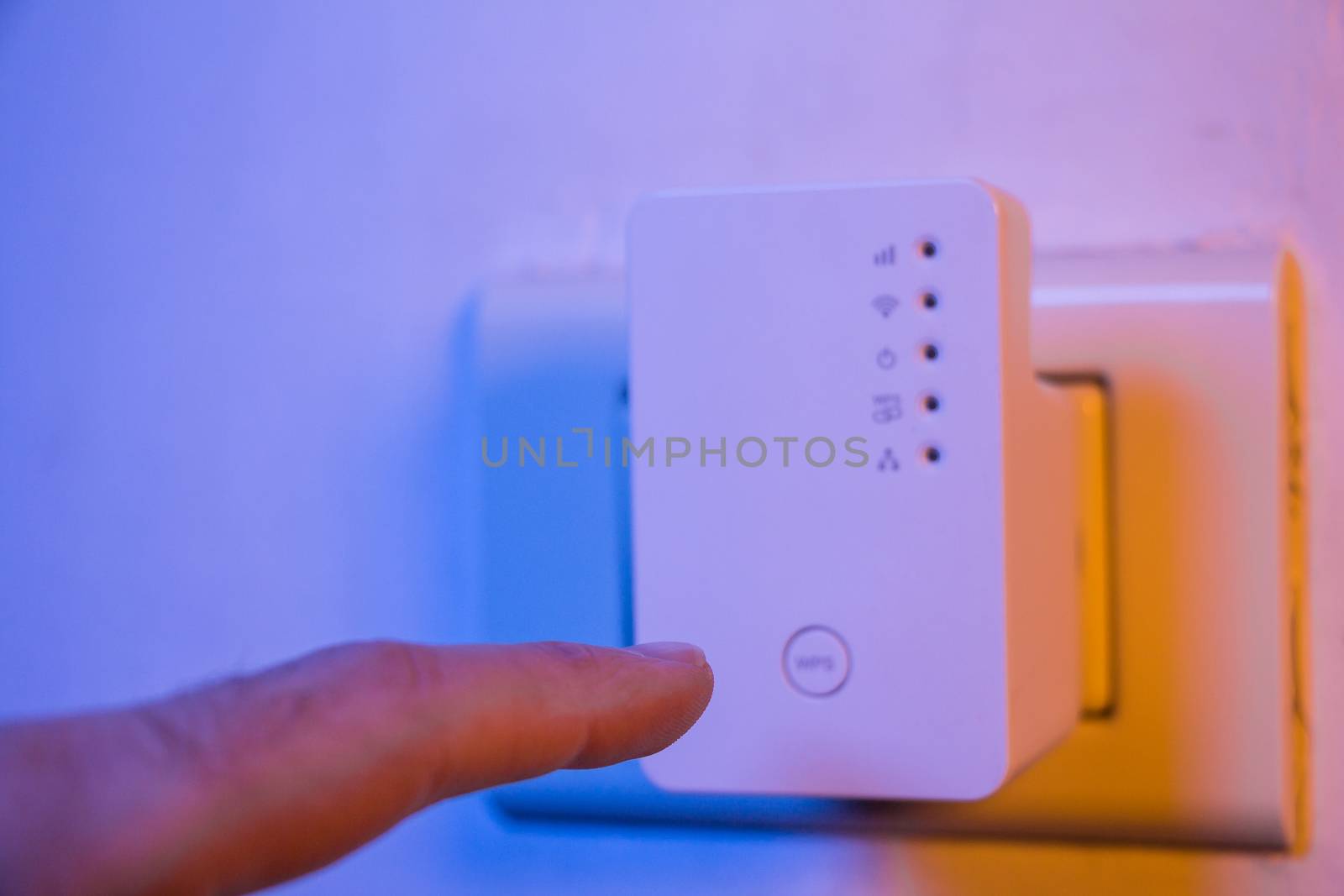 Man press with his finger on WPS button on WiFi repeater which is in electrical socket on the wall. The device help to extend wireless network in home or office.