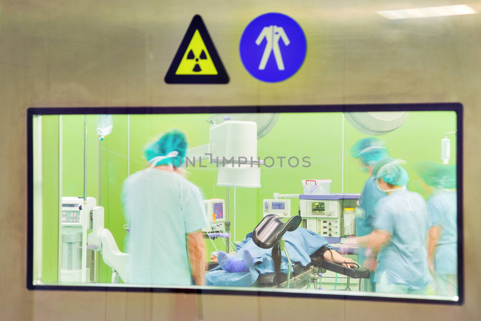 A view through the door window of a modern urology surgery with patient and motion blurred figures of doctors and nurses.