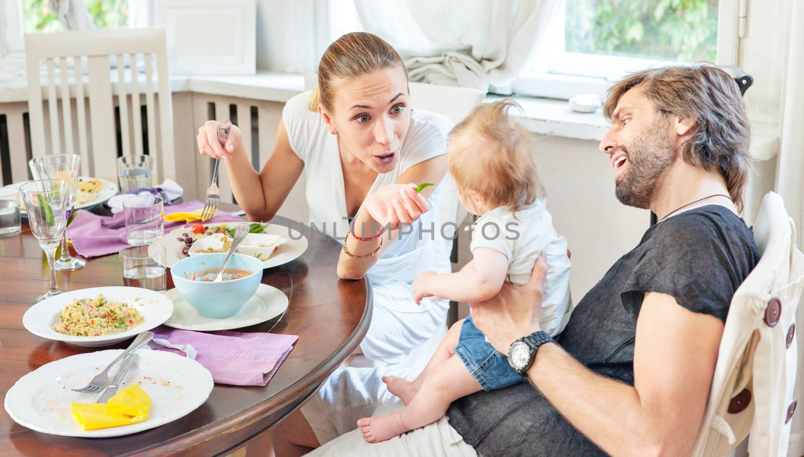 A happy family of young parents with a baby in restaurant.