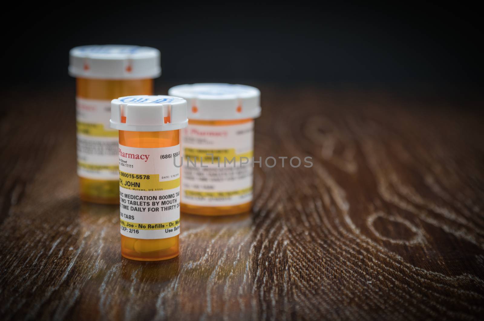 Variety of Non-Proprietary Prescription Medicine Bottles on Reflective Wooden Surface.