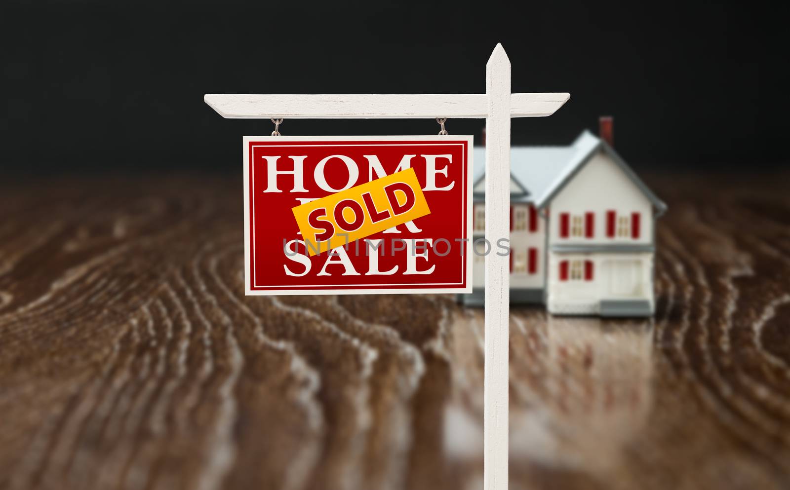 Sold For Sale Real Estate Sign In Front of Model Home on Reflective Wooden Surface.