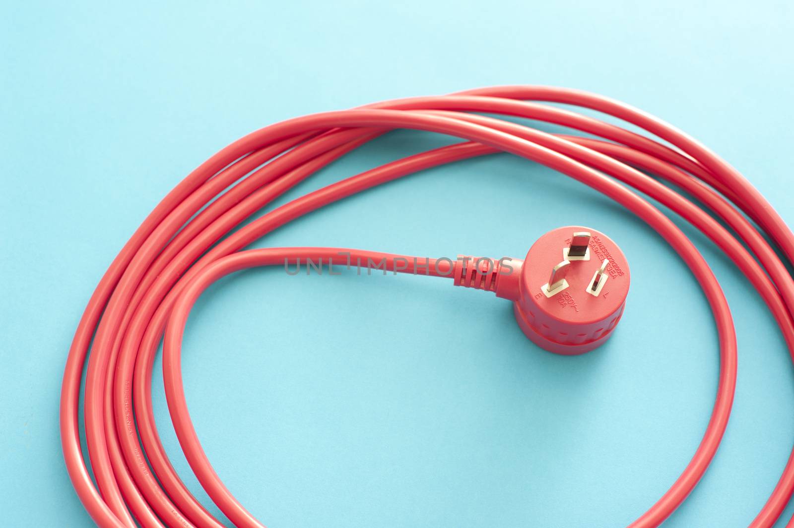 Long wound up red extension cord over blue background. Australian type plug receptacle.