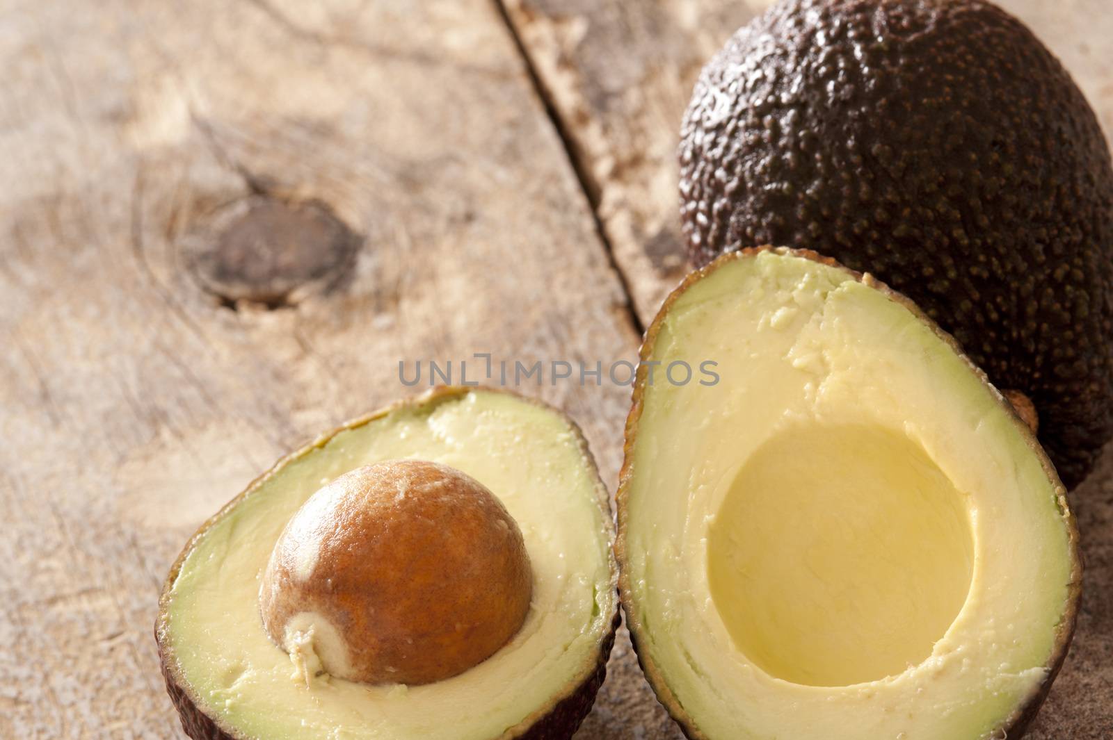 Pair of freshly cut and whole avocados on old wooden table with copy space over knot