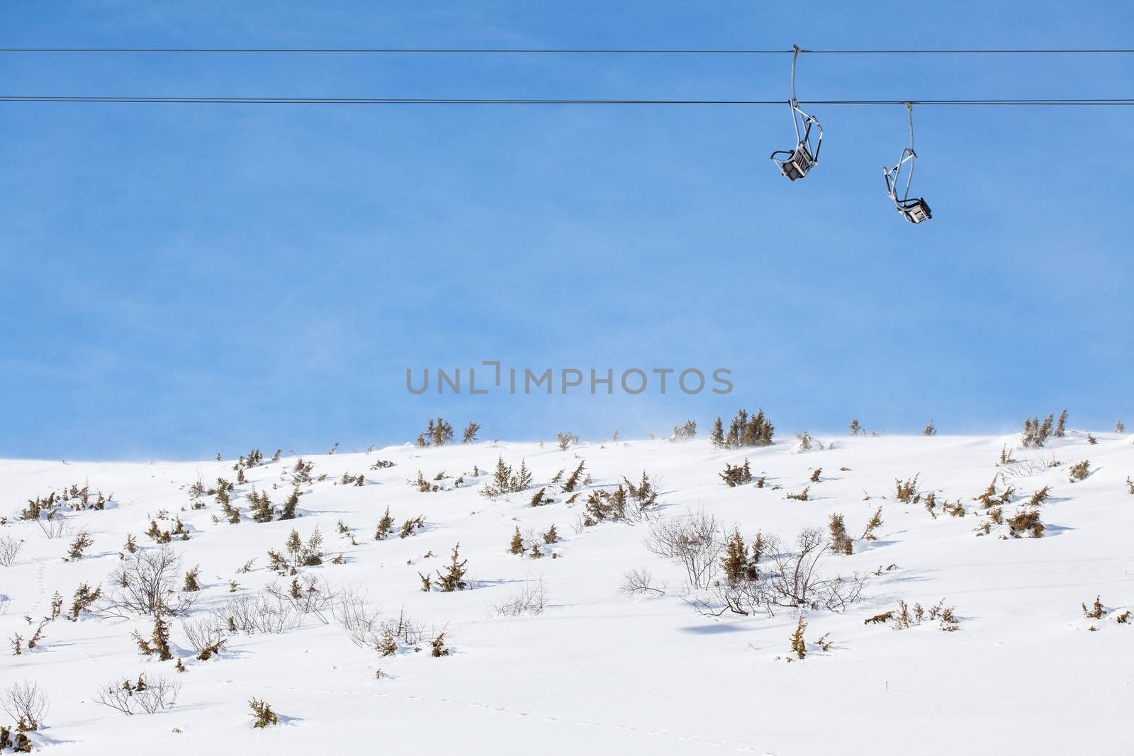 ski chair lift with two double seats, against blue sky, above snowy field