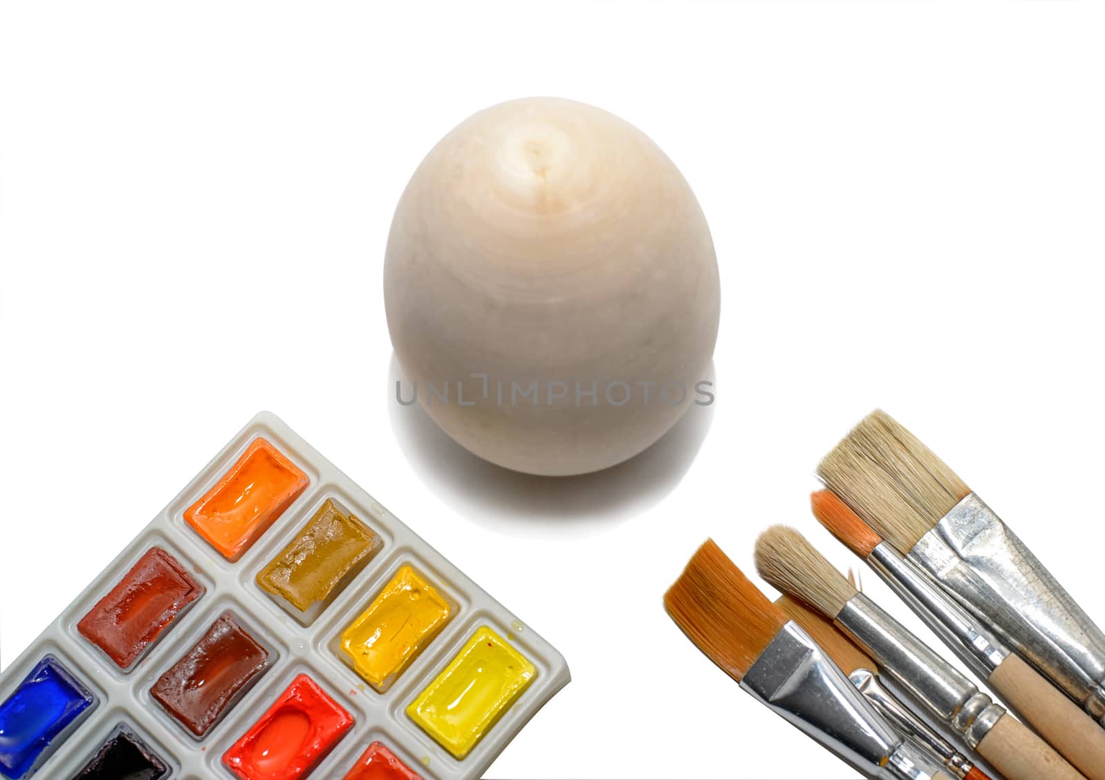 Wooden not painted egg on the background of a rainbow and a brush with paints, the concept of coloring the world with paints.