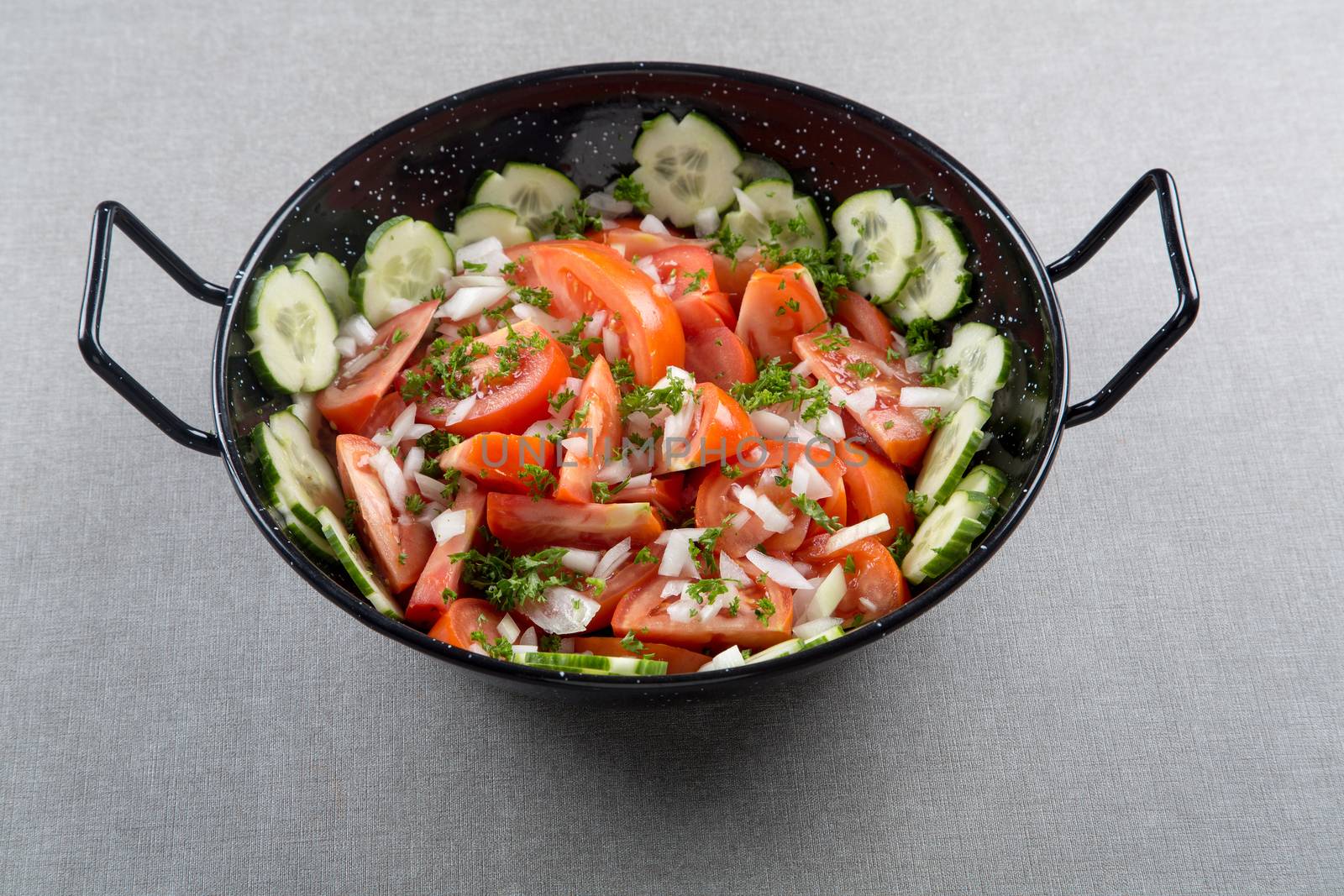 A bunch of sliced red tomatoes with cucumber and onion in a round metal bowl