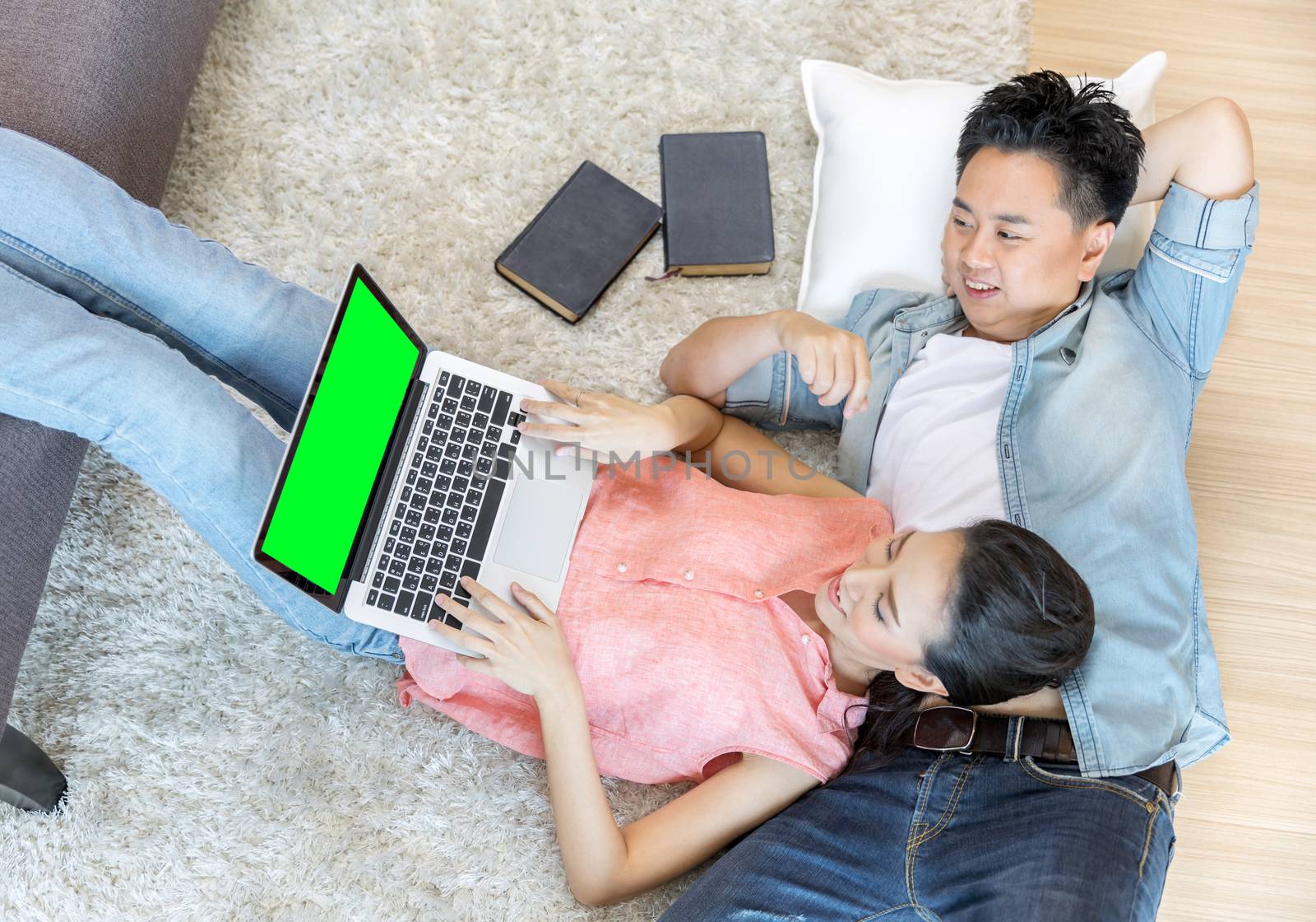 Young Asian Couples lying down and using laptop together in living room of contemporary house for modern lifestyle concept