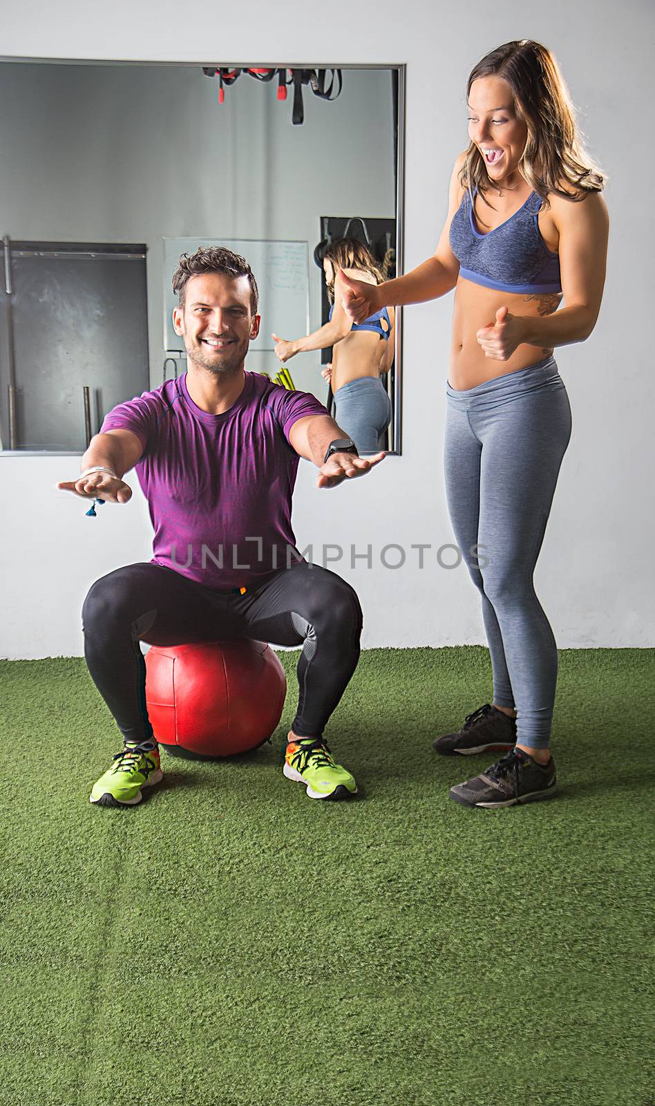 Young woman encouraging a man sitting on a red medicine ball