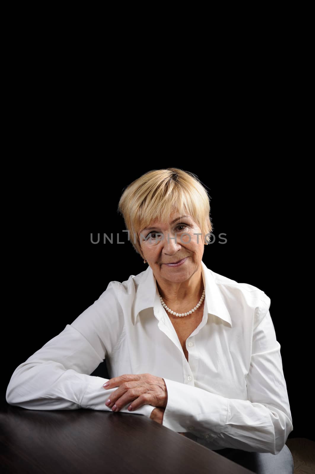Portrait of an elderly woman (70+) in a business suit against a dark background 
