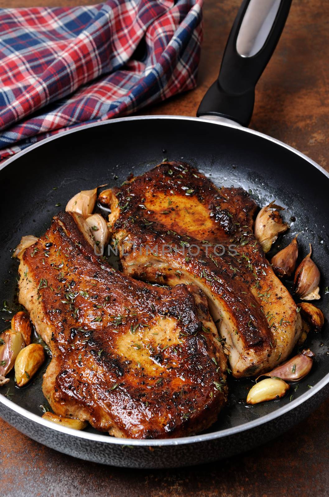 Fried pork chop on bones with herbs and garlic in a frying pan