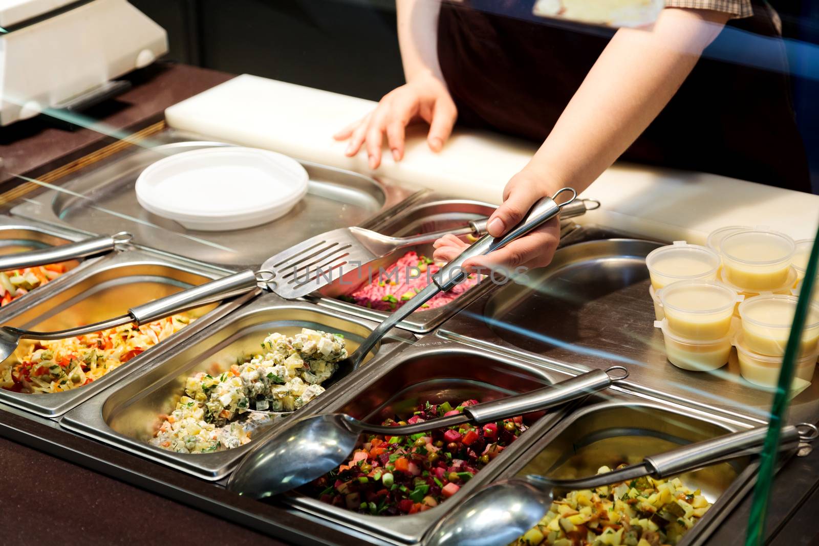 Trays with cooked food on showcase at cafeteria. Salad variety a by Nobilior