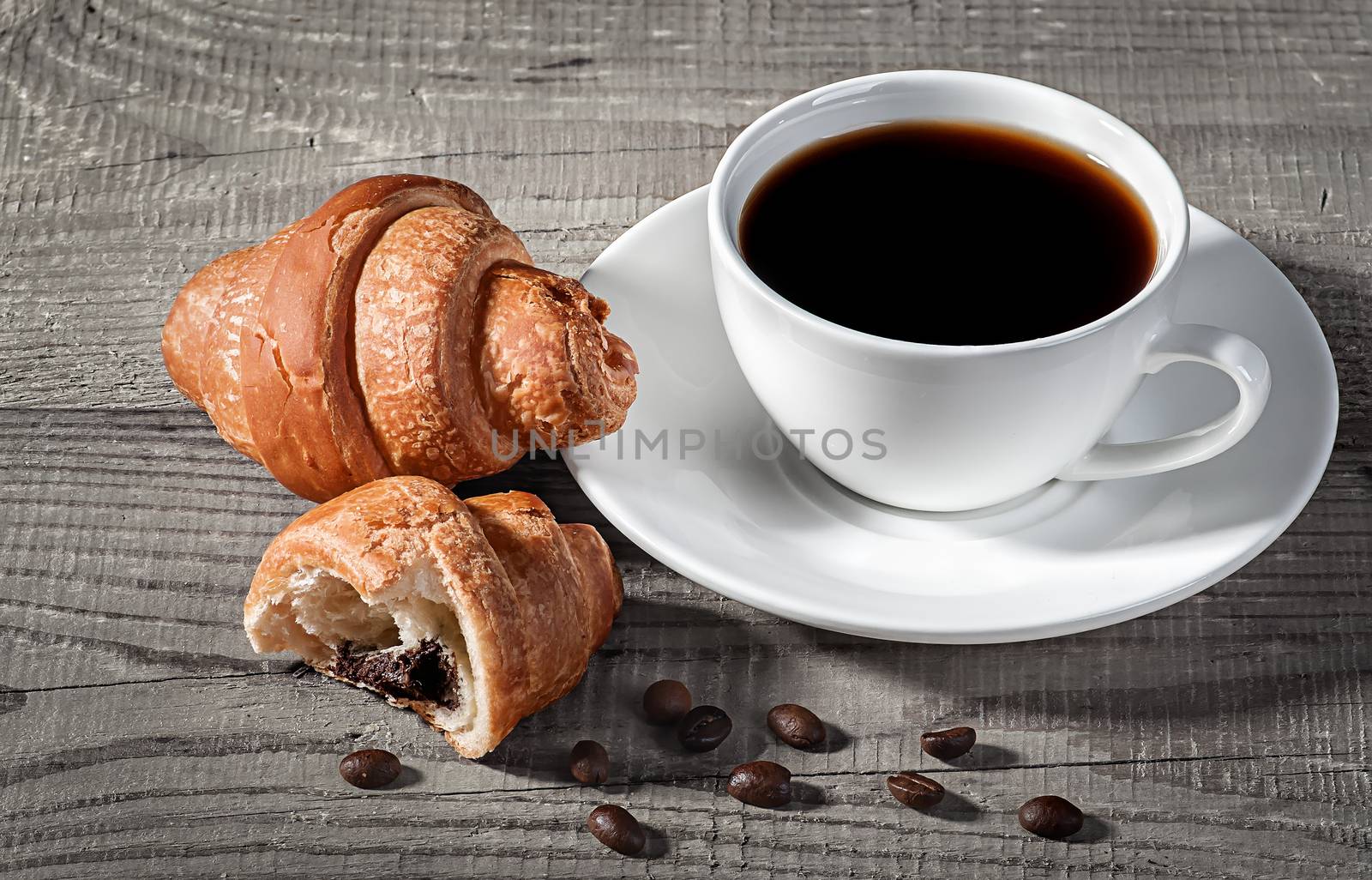 Coffee and croissants on a wooden table. Broken croissant and coffee beans nearby.