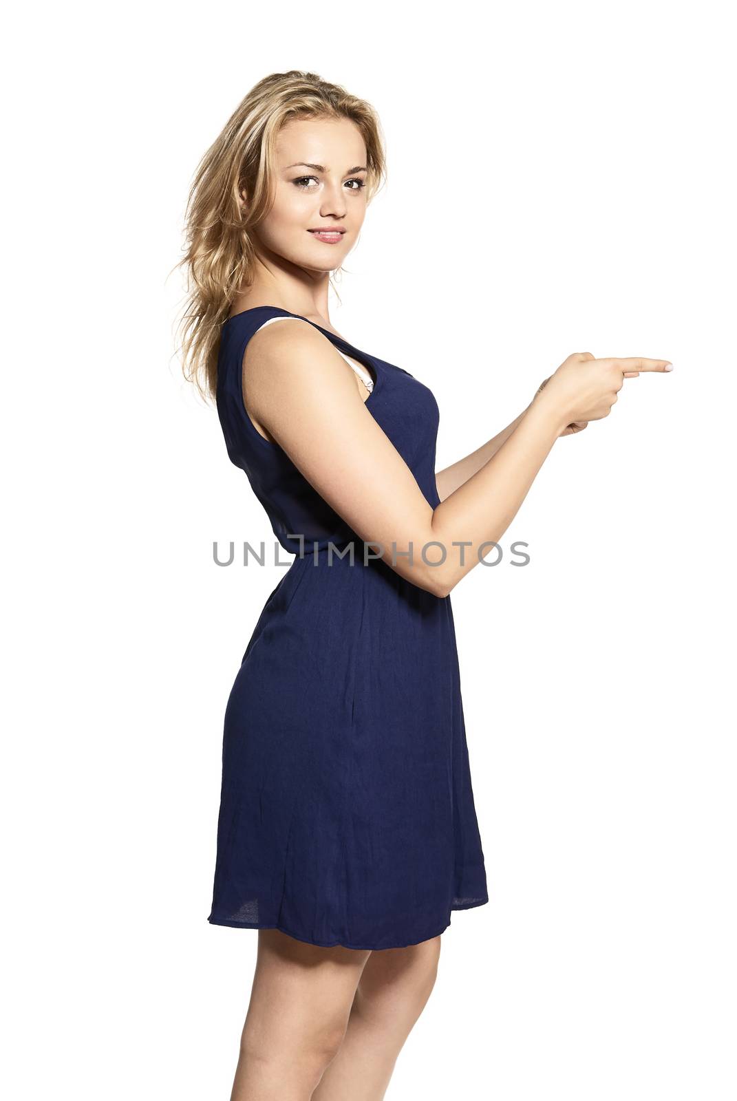 Portrait of positive smiling female wears navy blue dress against white background, points at copy space for your promotional text. Advertising concept.