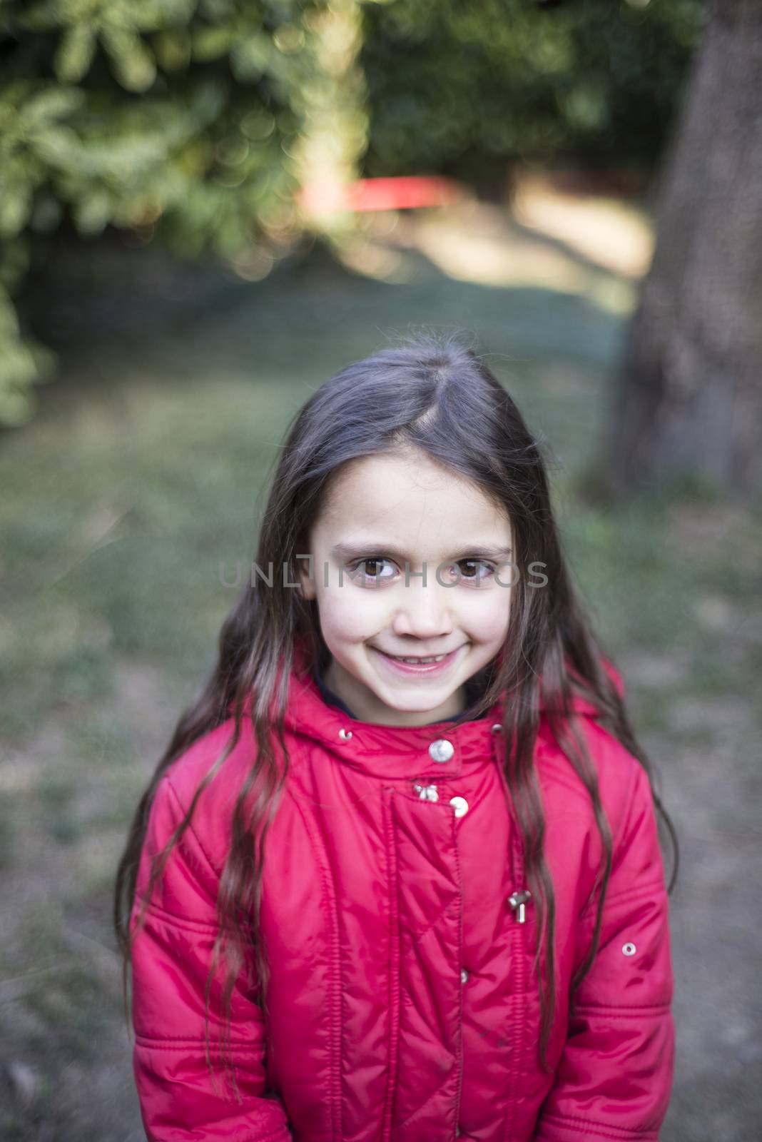 portrait of 7 year old girl in outdoor in the garden in winter with red jacket