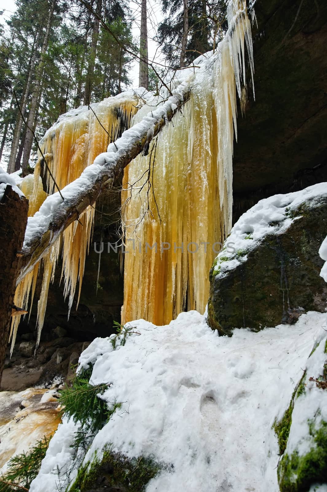 Frozen waterfalls on the rock, orange colored and snow