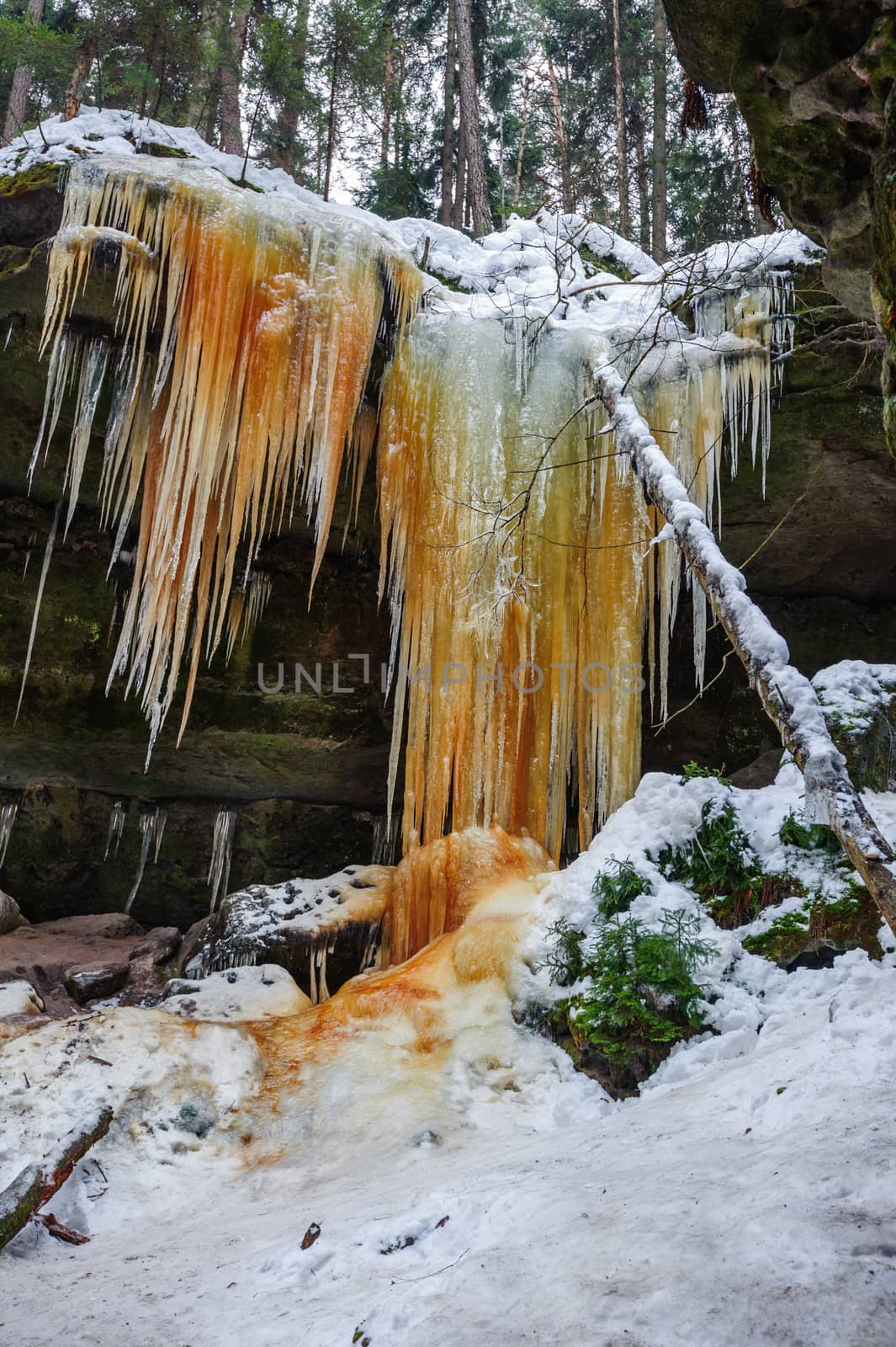 Frozen waterfalls on the rock, orange colored and snow