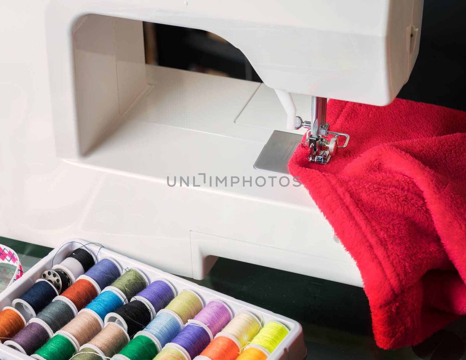 sewing machine and red cloth, sewing process in the phase of overstitching,colored spools.