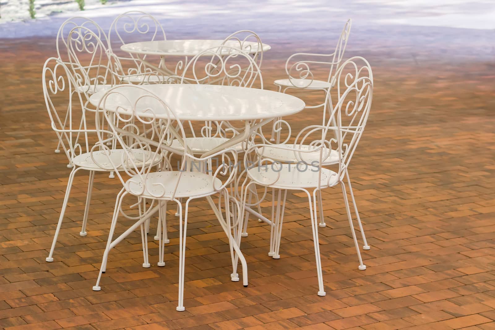 White metallic tables and chairs with openwork backs on the floor made of a brown tiles in summer cafe
