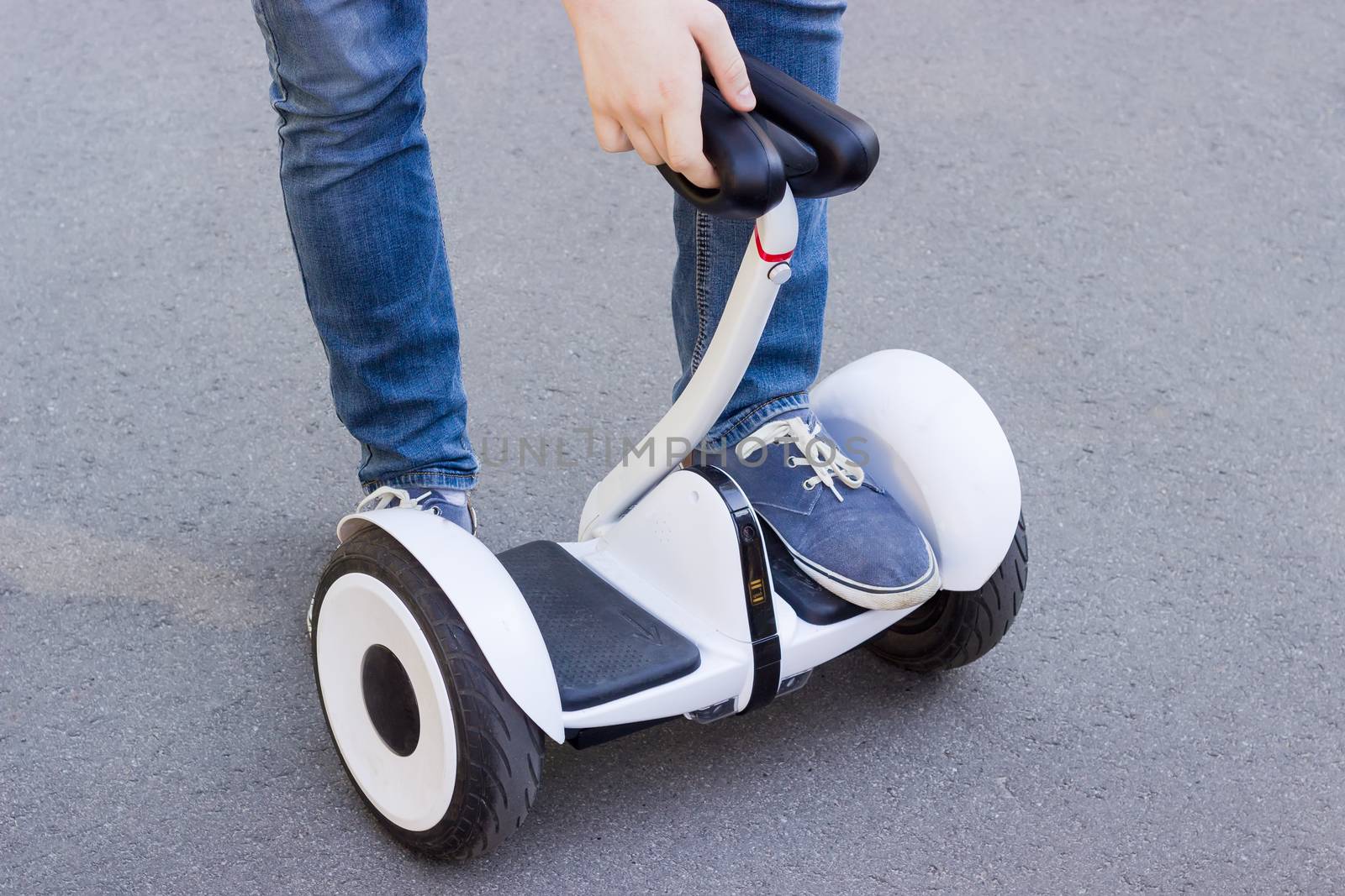 Legs of young man in blue jeans stepping on a segway on a asphalt surface
