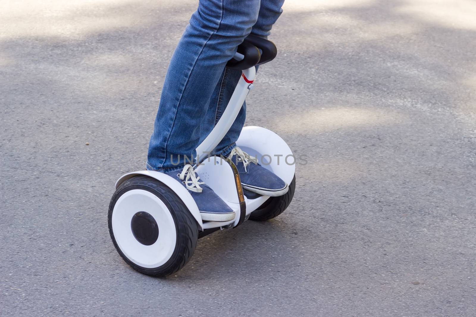 Legs of young man in blue jeans riding a segway on the asphalt walkway
