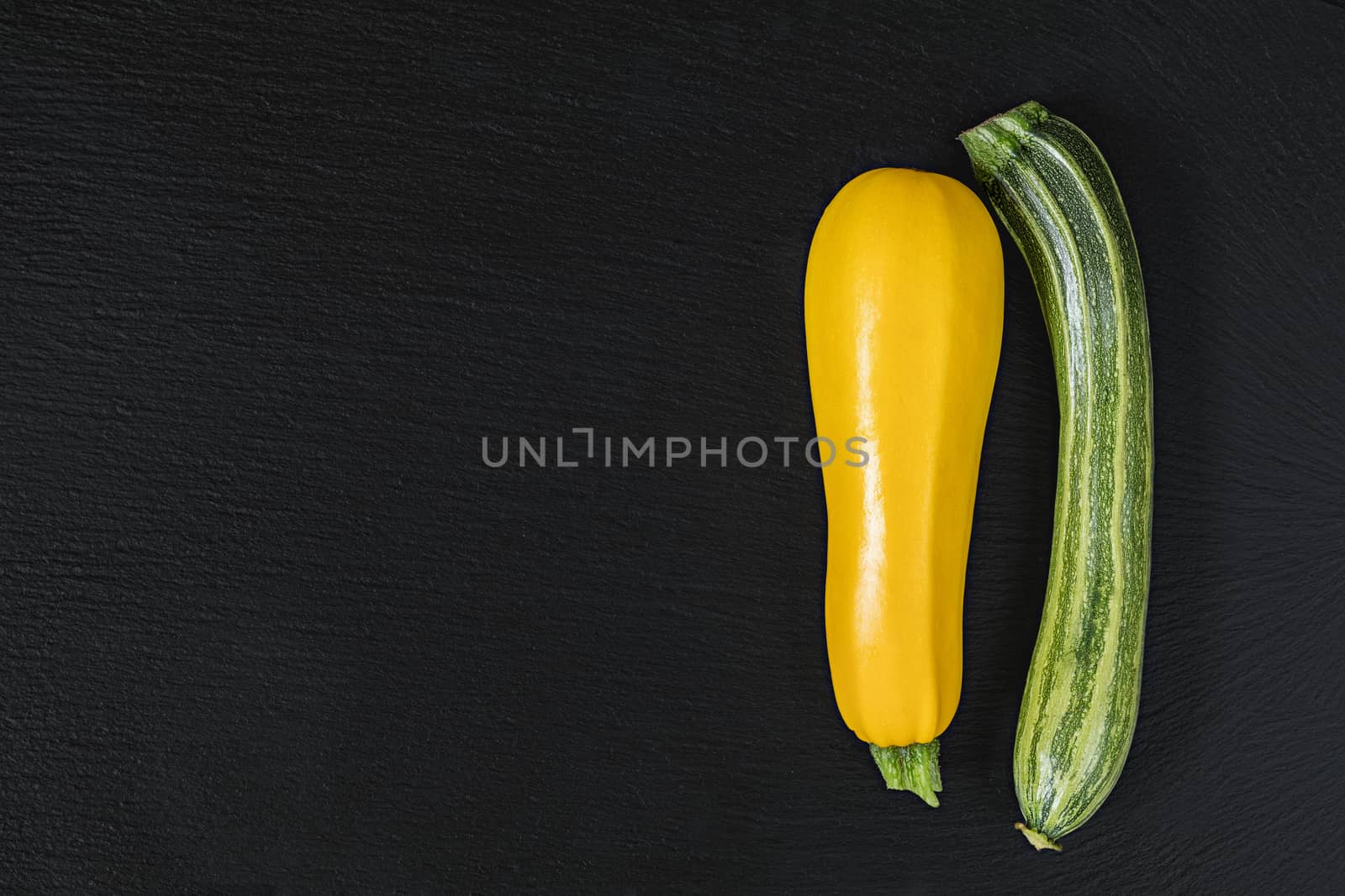 Striped fresh green zucchini and yellow zucchini on a black stone surface.  Top view, copy space. Healthy eating concept.