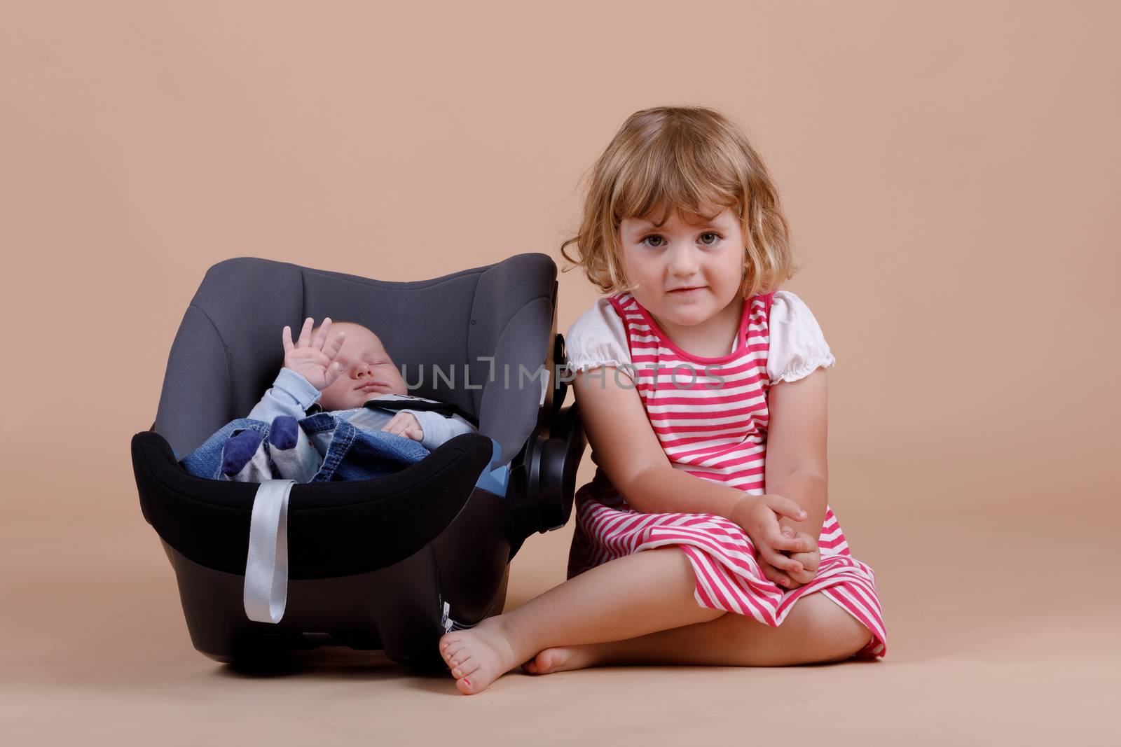 studio portrait of young cute baby girl with infant brother on beige background