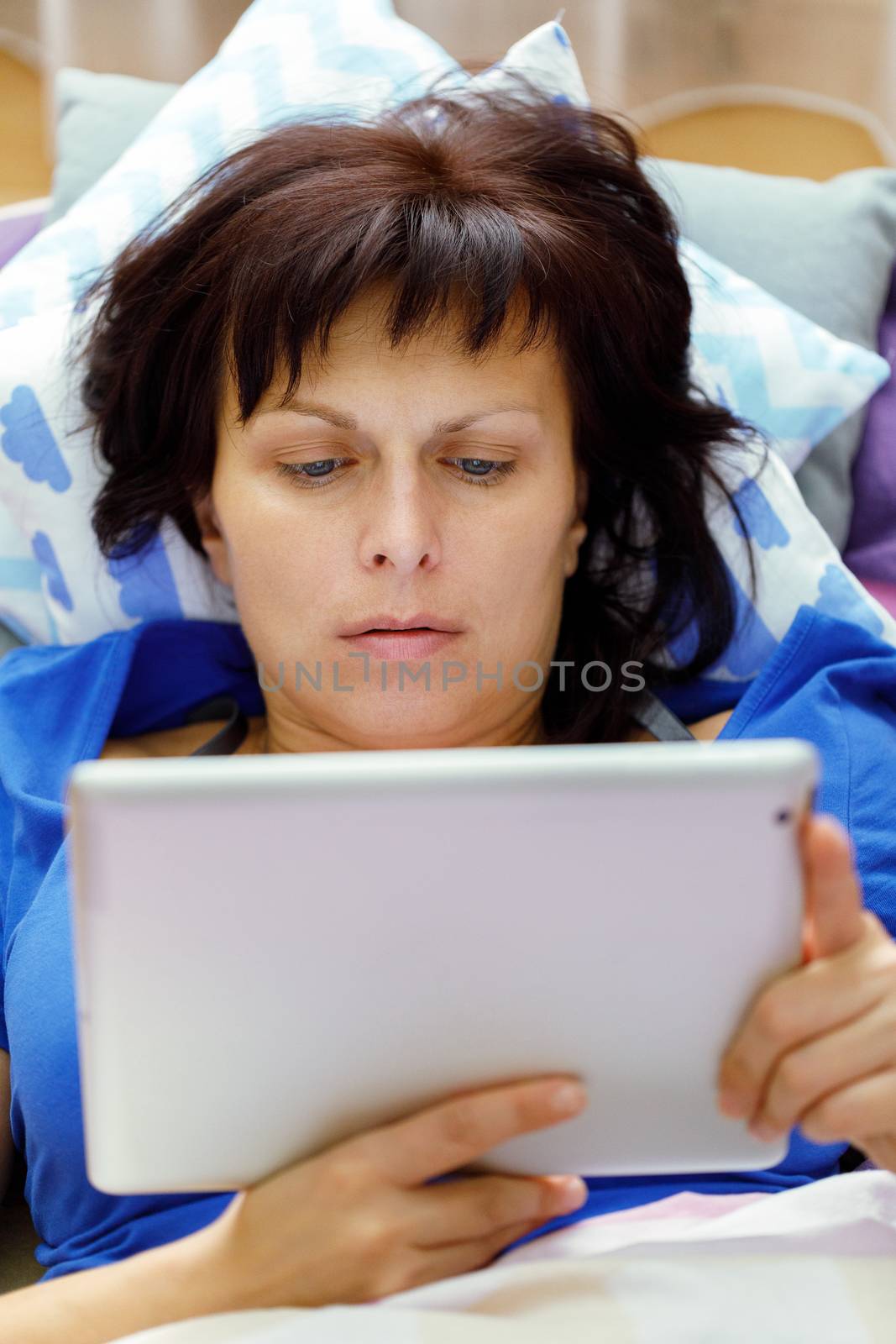 Middle age woman resting in bed with tablet computer and reading news