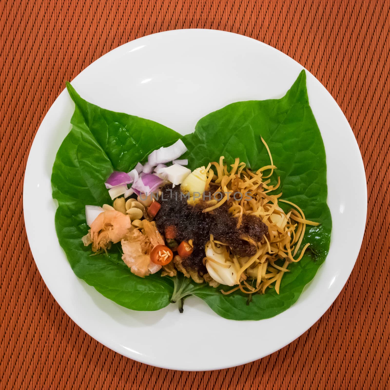 The close up of Thai appetizer leaf wrapped with herbs (Miang Kham) on white plate.