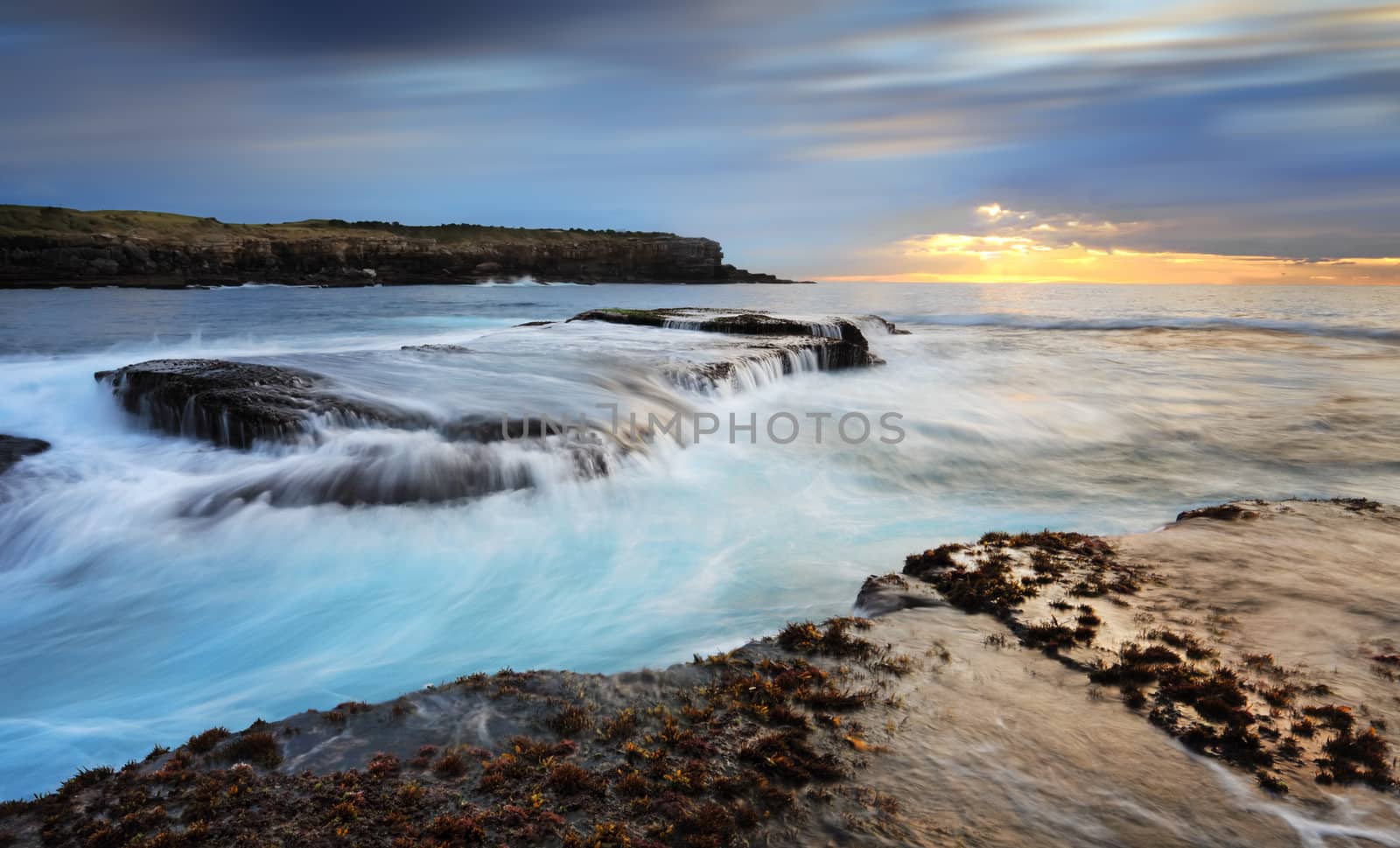 Fast flowing ocean waves over and around rocks in the low tide at Little Bay Australia