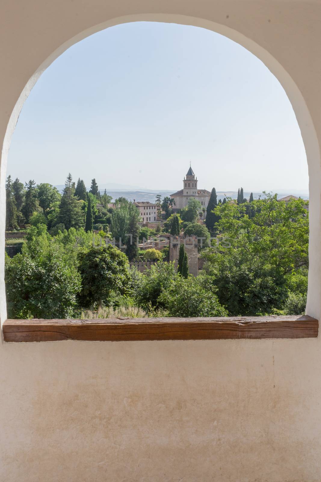 View of the bell tower of the Alhambra through the arched window from the Generalife gardens in Granada, Spain, Europe on a bright summer day