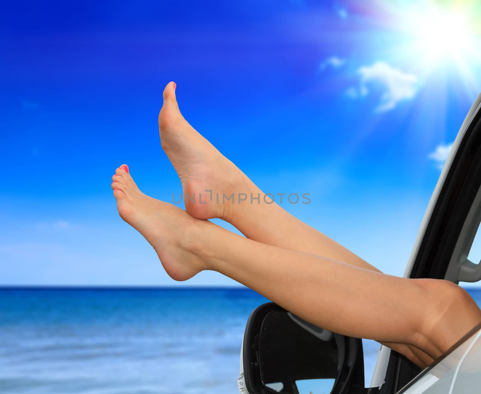 Beaitiful female legs against the sea and summer blue sky. Vacation, travel summer holidays concept. Woman shows her slim legs from the car window