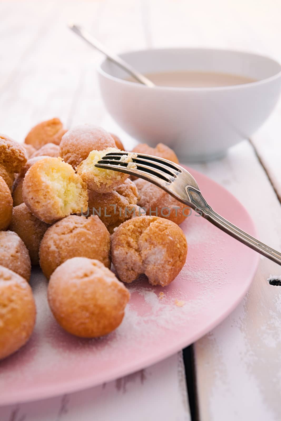 Closeup of castagnole, typical Italian carnival sweet on a pink plate with milk and coffee cup
