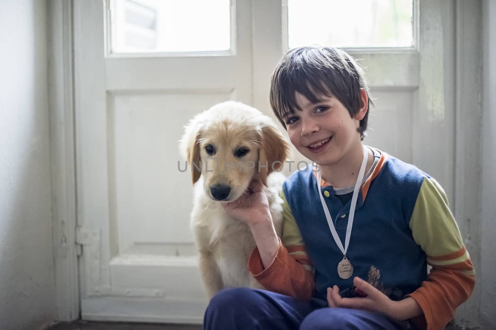 6 year old boy in pajamas with his golden retriever puppy dog in the house in front of the hall window