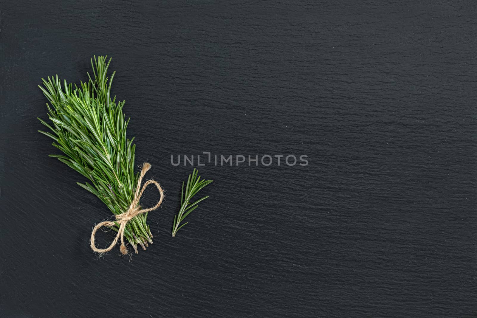 Rosemary bunch of bouquets on black stone surface. Top view, copy space.