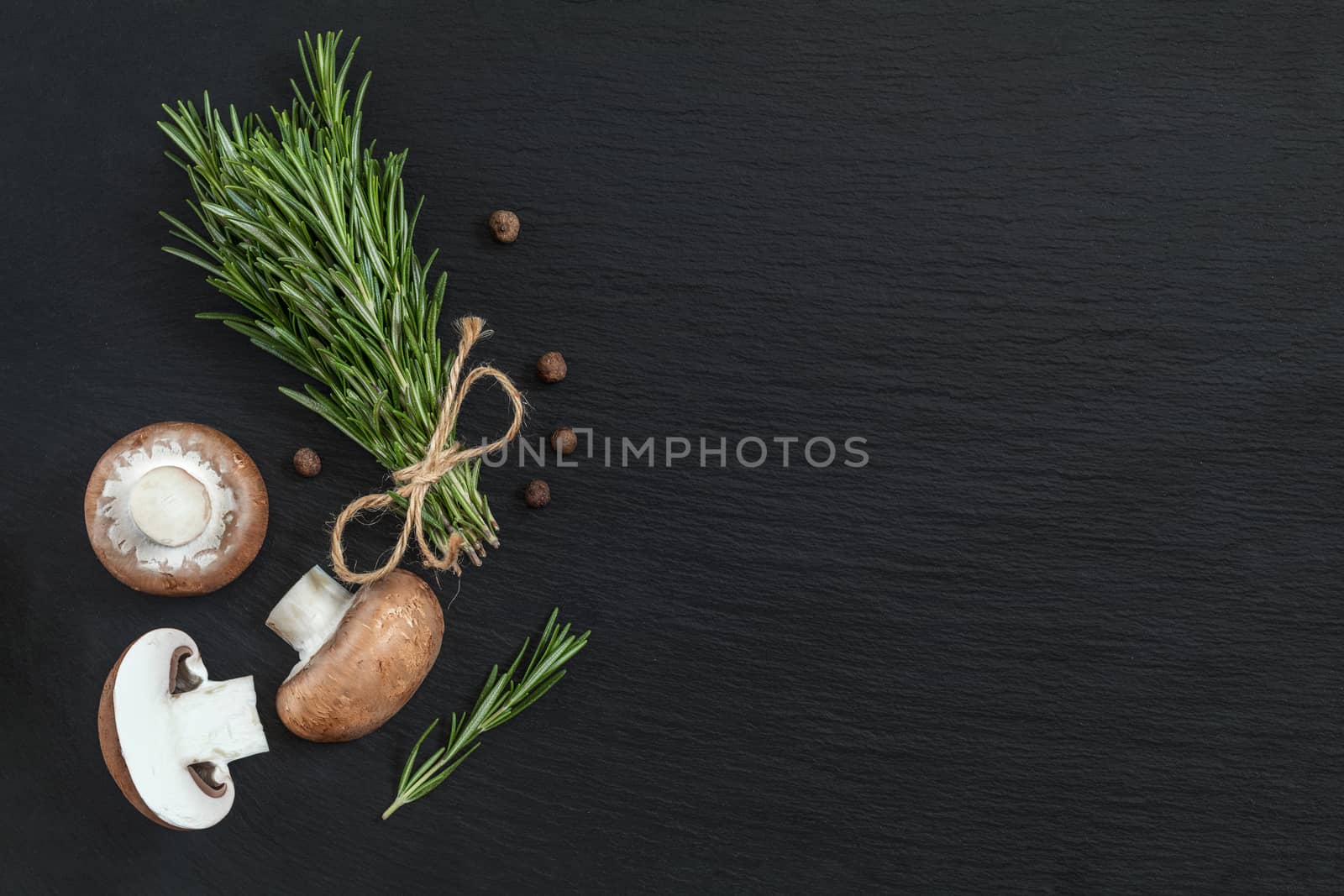Rosemary bunch of bouquets, mushrooms and fragrant pepper on black stone surface. Top view, copy space.