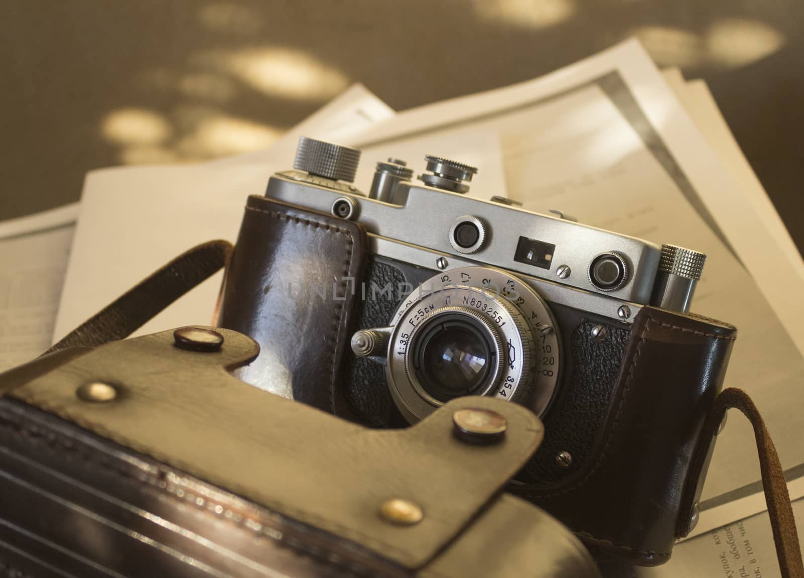 Old Soviet camera in soft sunlight. Vintage camera in a leather case on paper background.