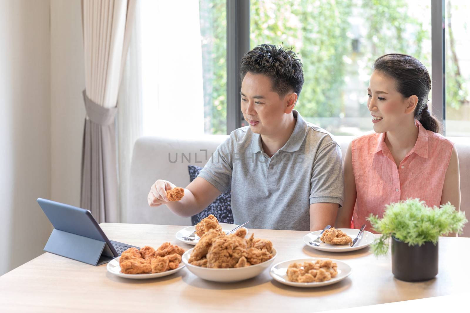 Young Asian Couples eating fried chicken together in living room of contemporary house for modern lifestyle concept