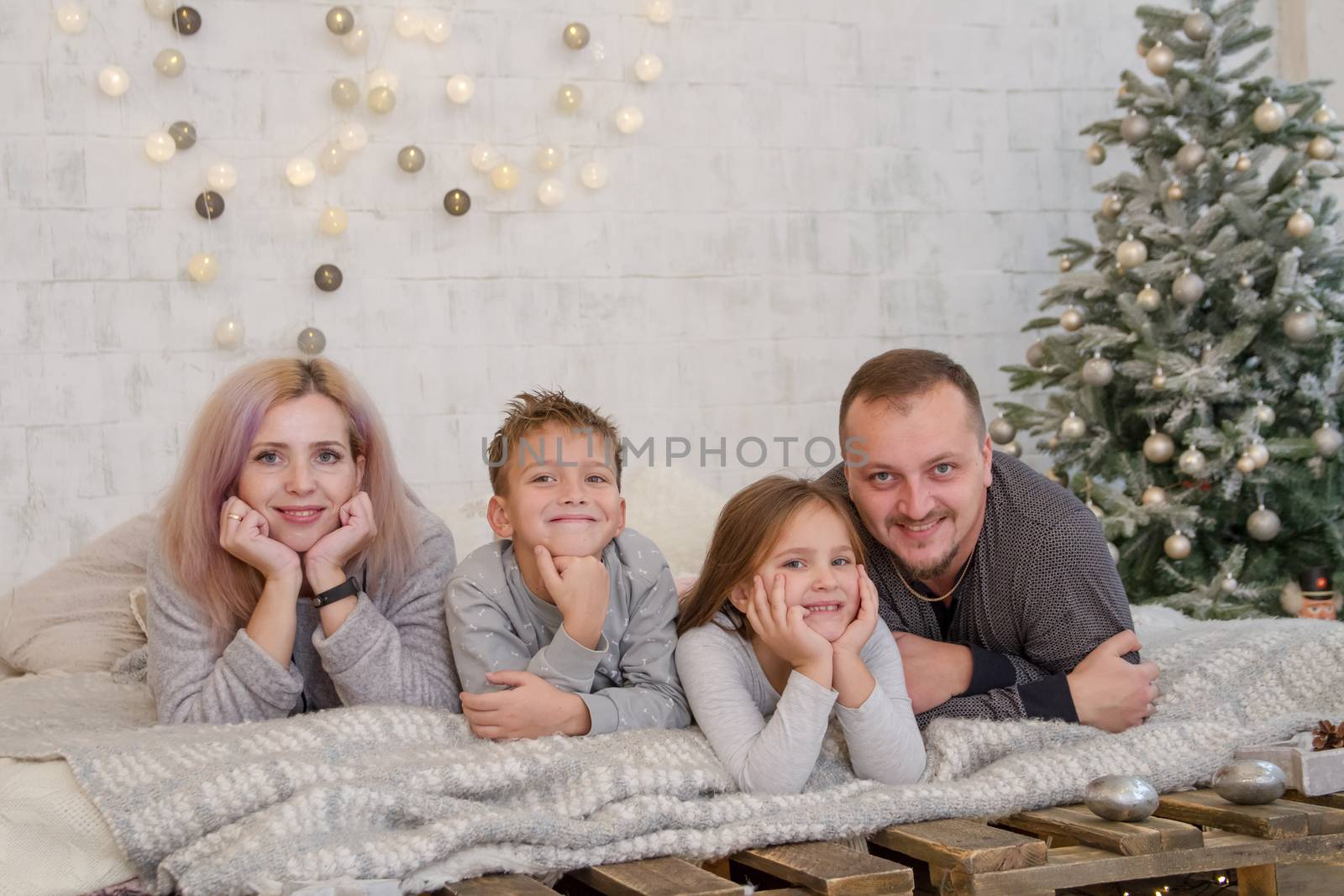 Happy family with two children under Christmas tree lying on bed