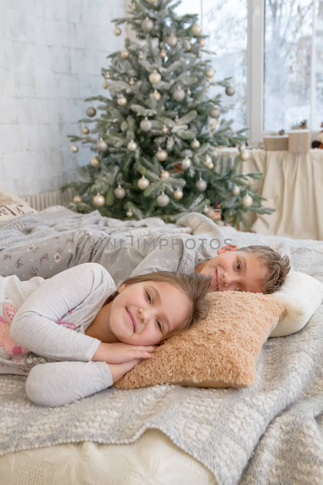 Sister and brother lying on bed under Christmas tree