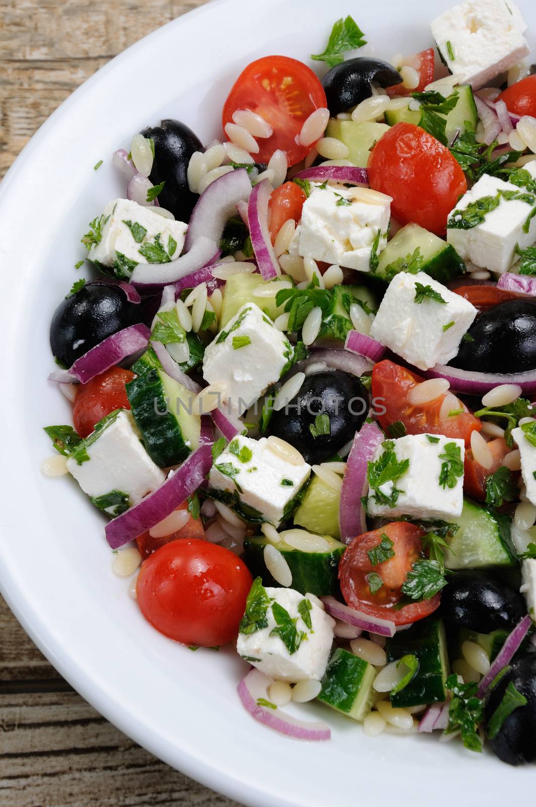 Greek salad orzo pasta with black olive, red onion and cucumber, cherry tomatoes, feta and herbs. Vertically shot. View from above