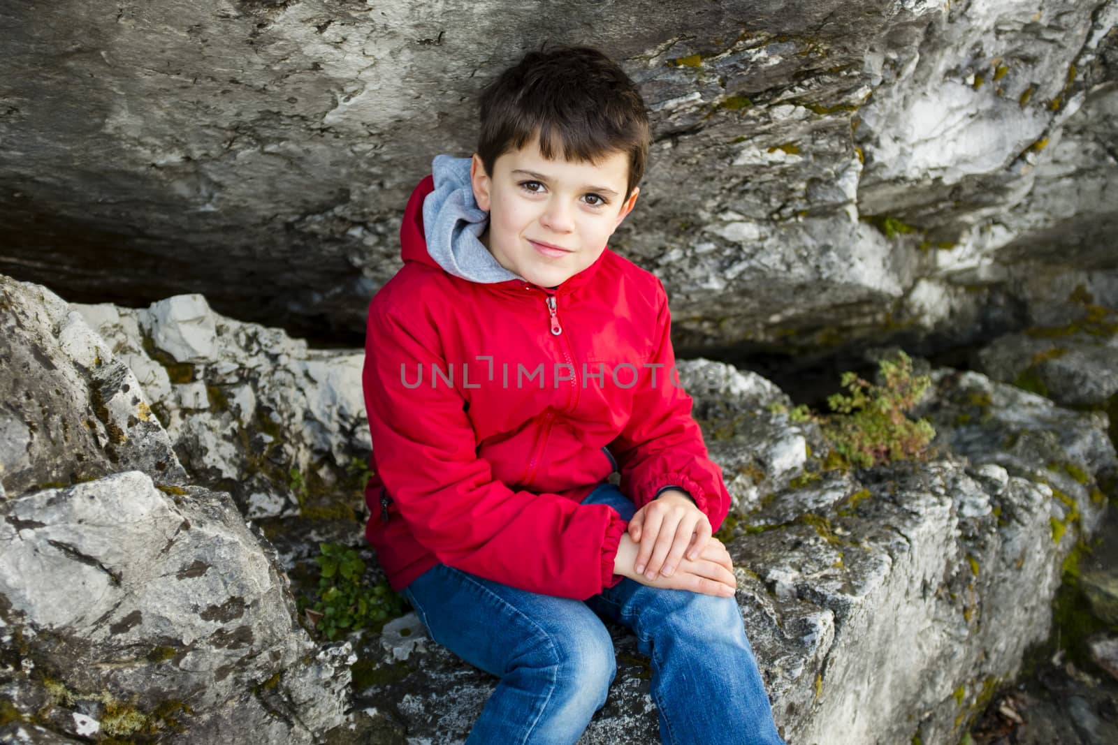 portrait of 9 year old boy with red jacket outside, as a big rock background